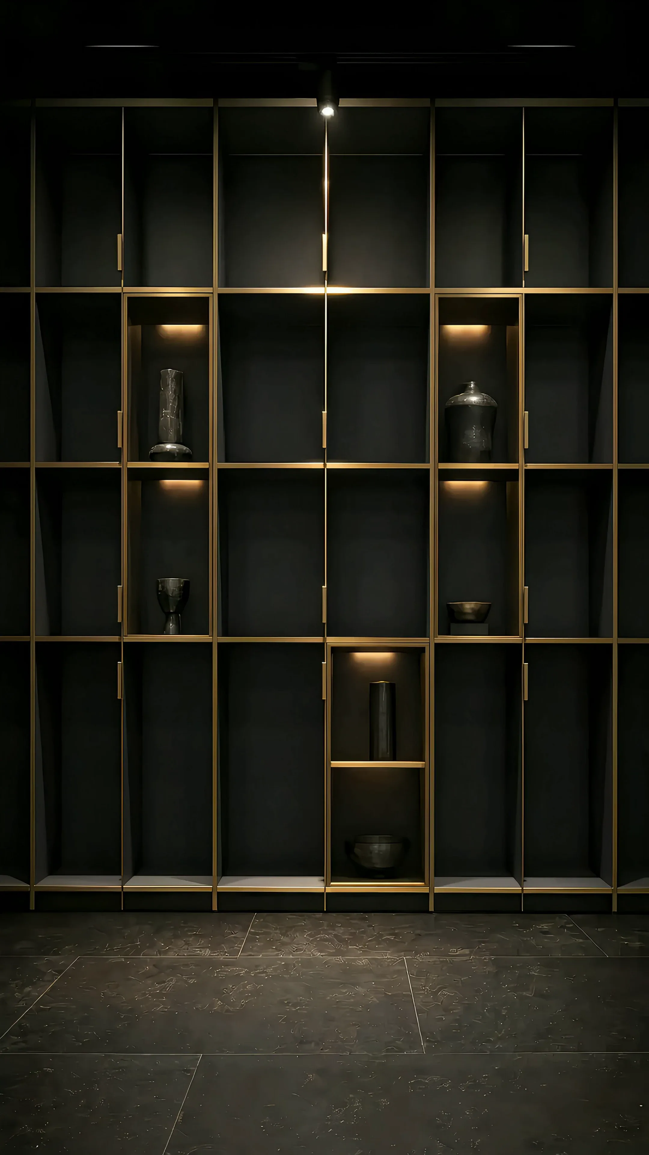 A floor to ceiling fitted storage wall in charcoal on a brass grid, its niches lit from inside, on a dark stage