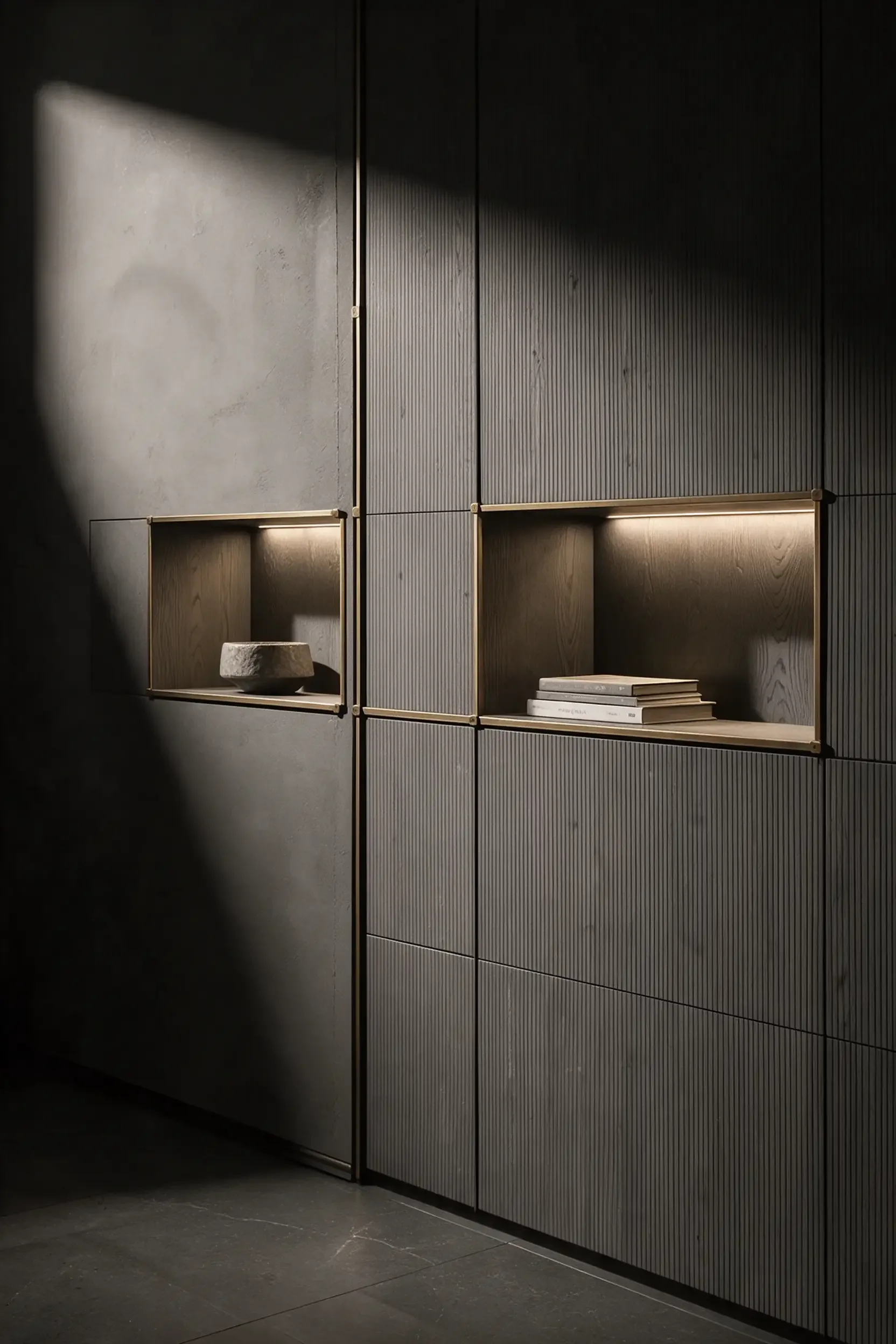 Lit niches in a fitted storage wall holding books and ceramics, brass trims on grey fronts