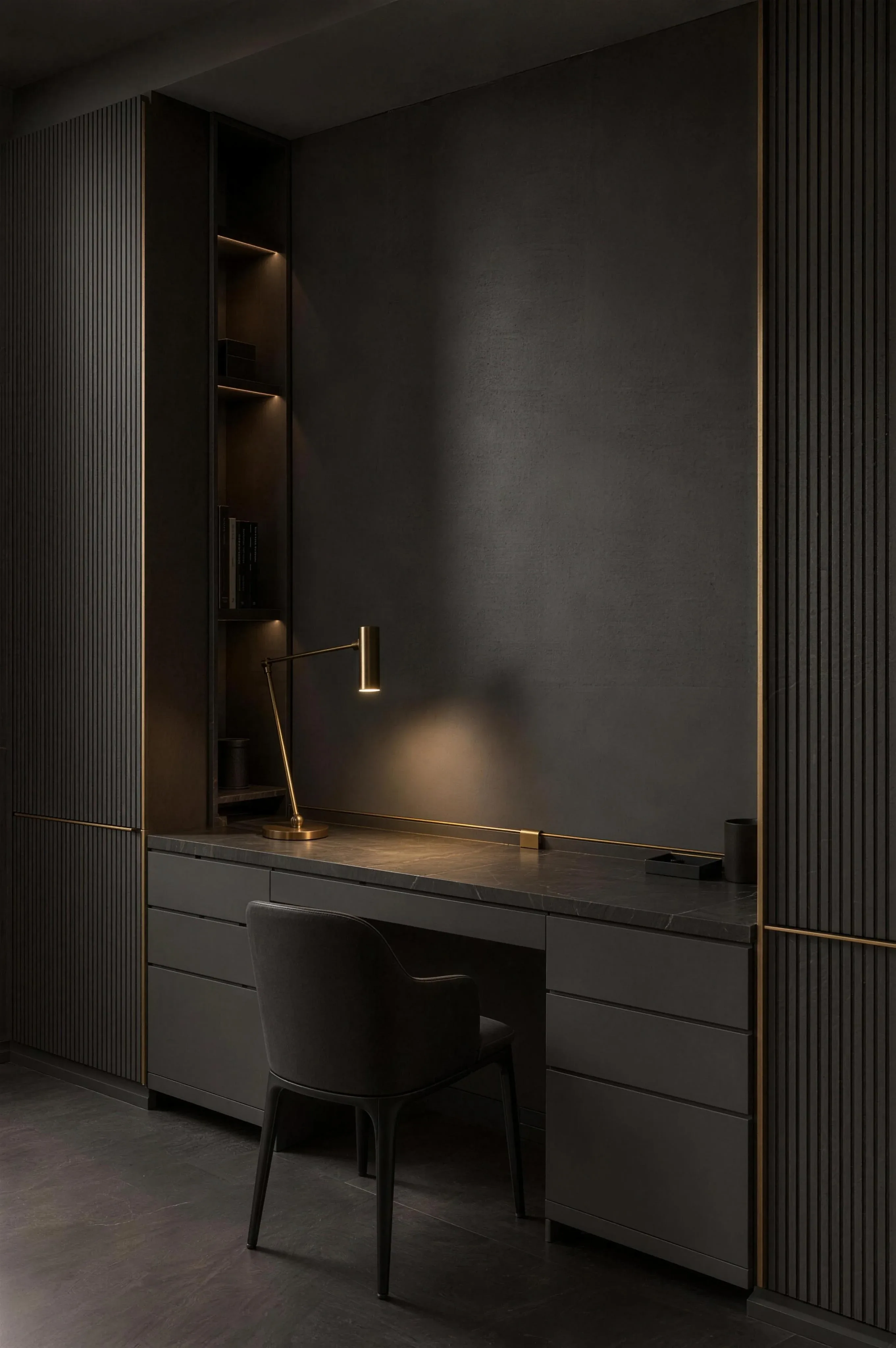 A fitted study wall in grey with a built-in desk, a brass task lamp and shelves lit from under