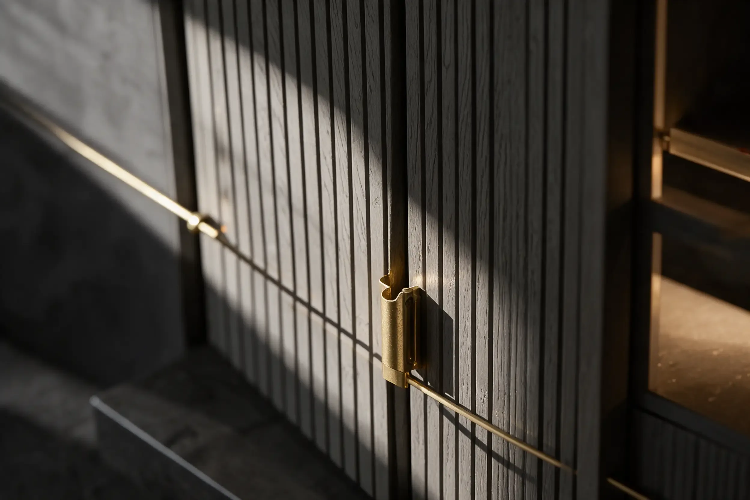 Fluted grey veneer wardrobe fronts with a slim brass handle in raking light